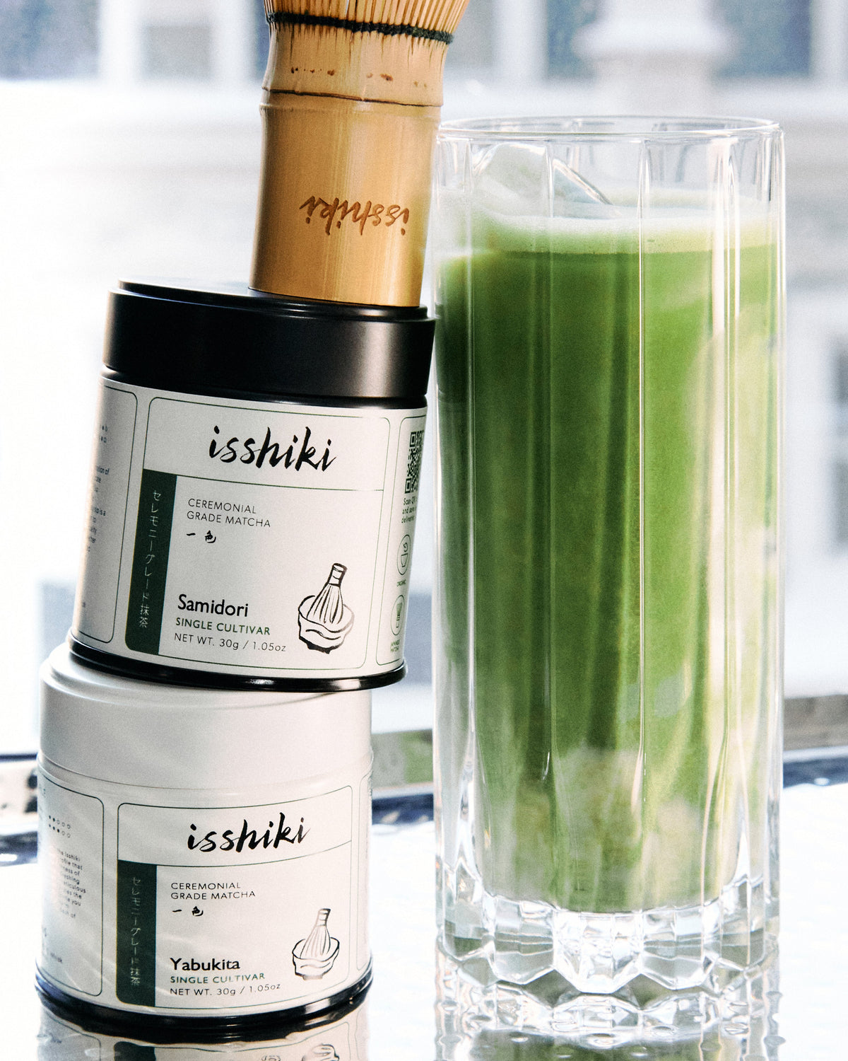 Isshiki Samidori matcha tins displayed beside a tall glass of iced matcha