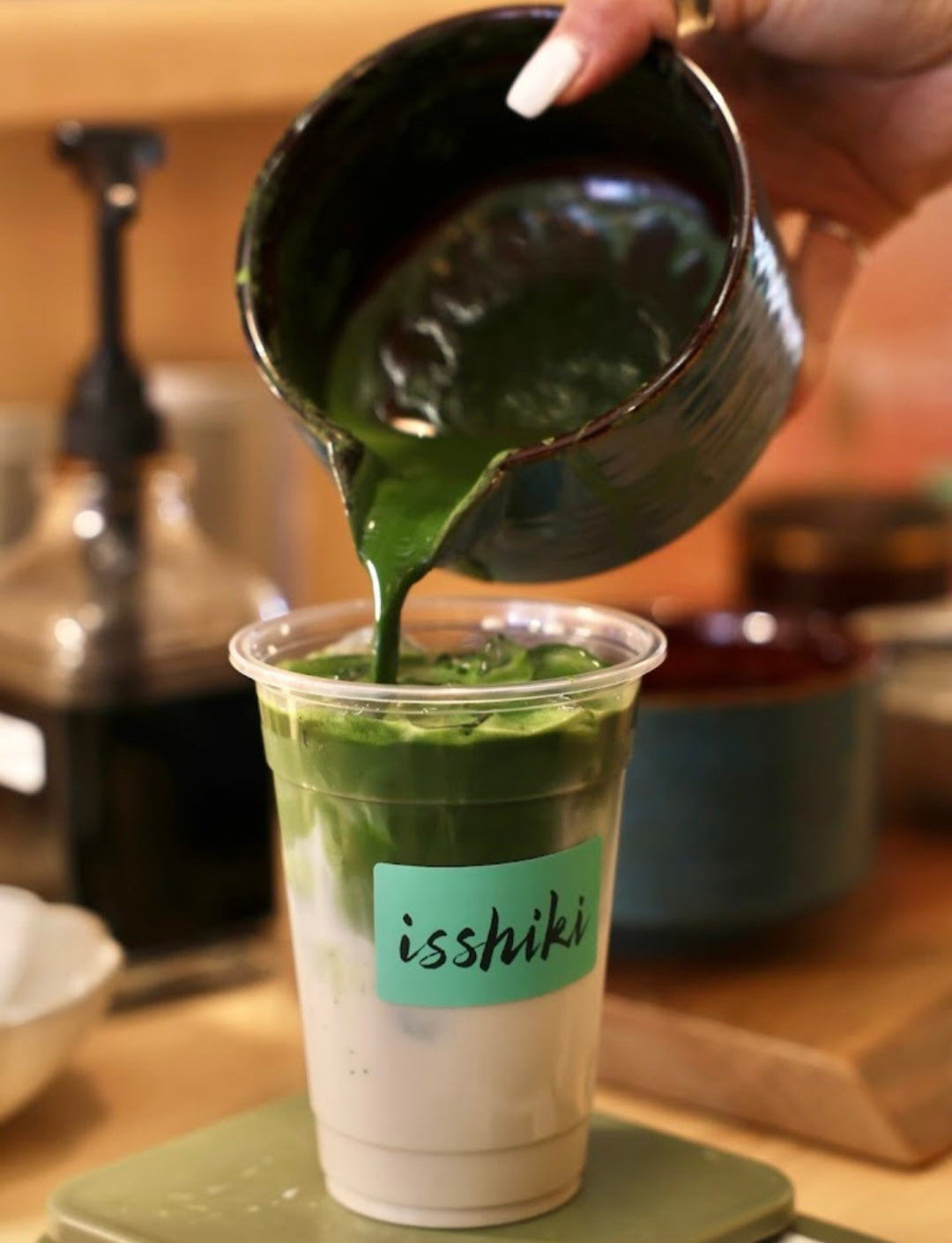 Pouring green matcha into an iced latte in a clear glass
