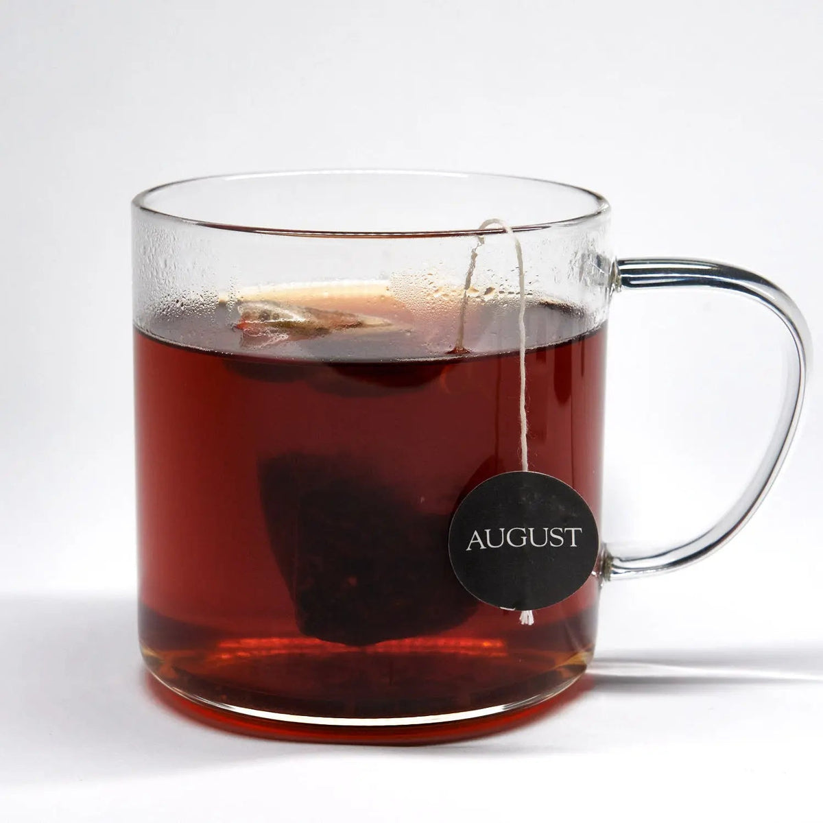 Glass mug filled with brewed August Dirty Chai black tea and a pyramid tea bag