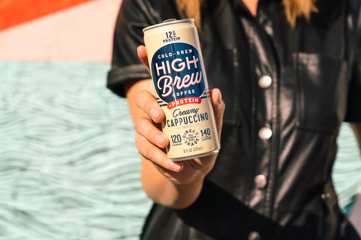Person holding a High Brew Creamy Cappuccino protein cold brew coffee can outdoors