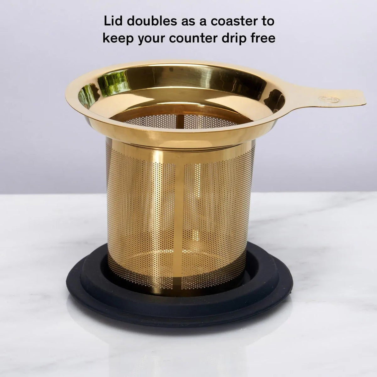 Gold stainless steel tea infuser resting on black silicone coaster
