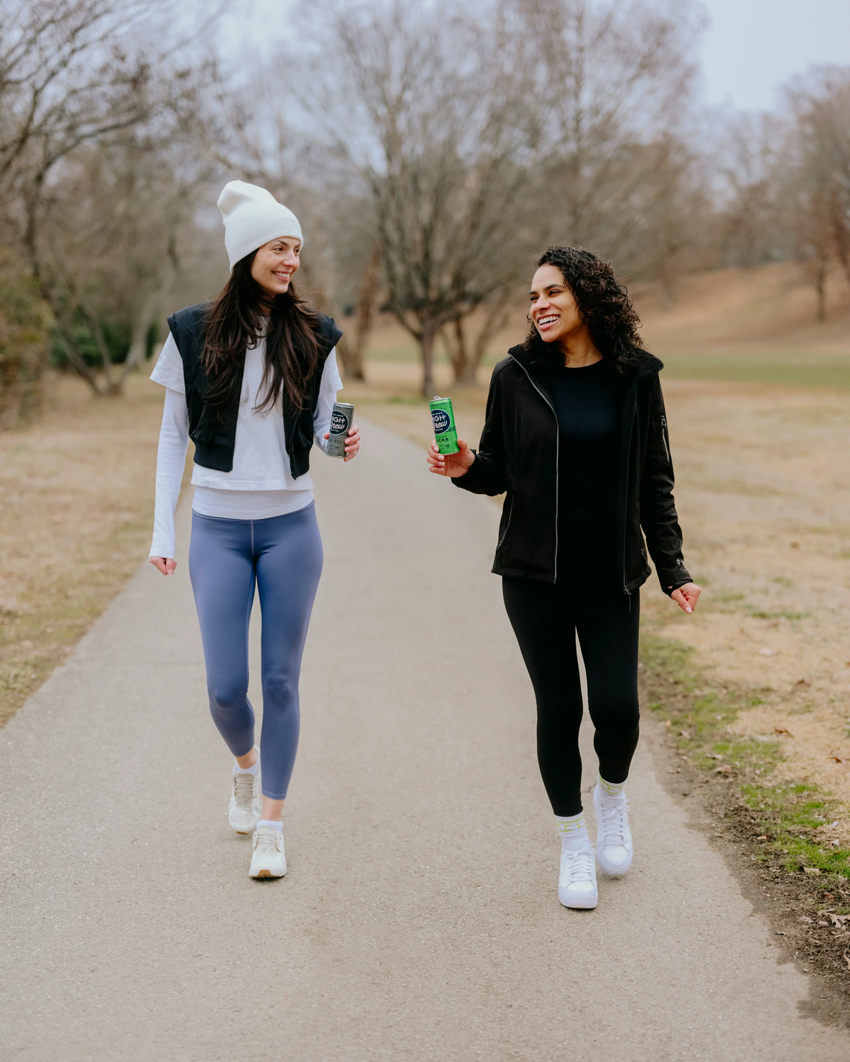Two women walking outdoors, one holding a High Brew cold brew coffee can