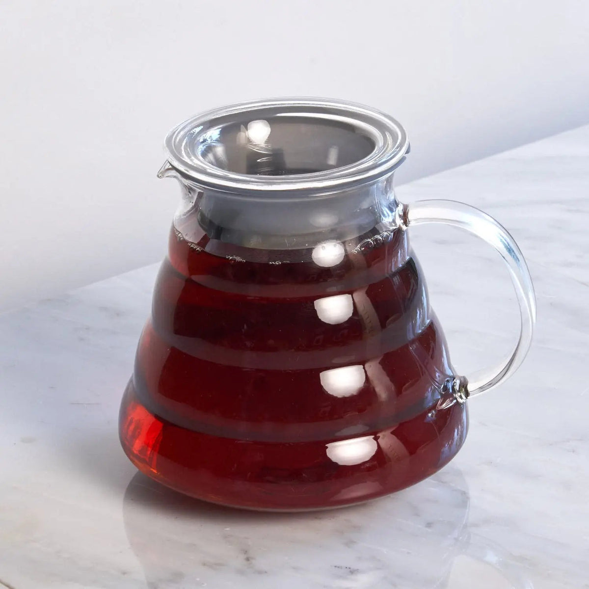 August clear glass teapot filled with amber-colored brewed tea and fitted with a stainless steel lid