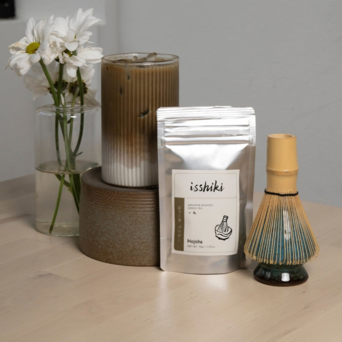 Isshiki Hojicha roasted tea powder displayed with bamboo matcha whisk and ceramic cup