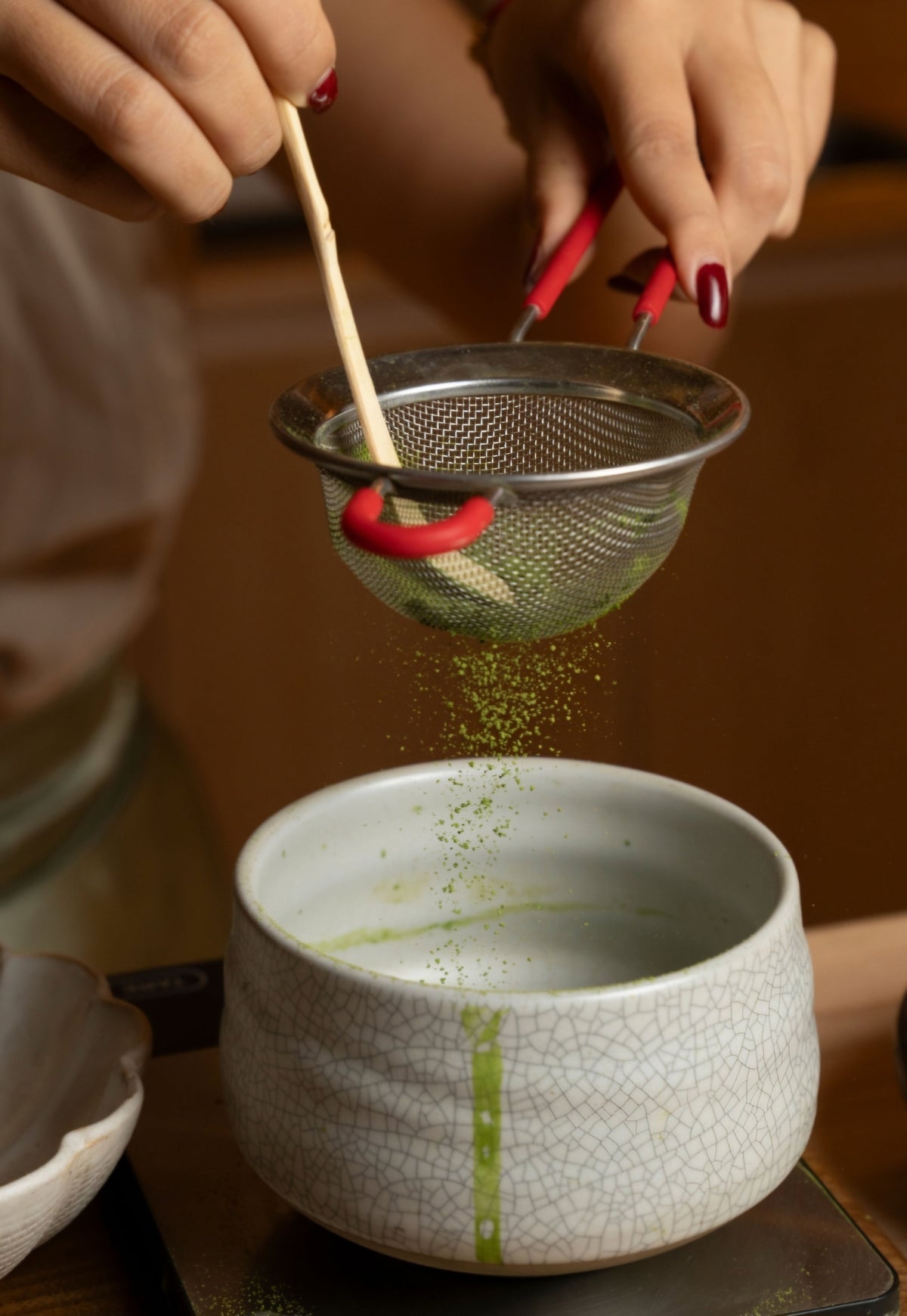 Fresh green matcha being whisked through a fine mesh strainer into a ceramic bowl