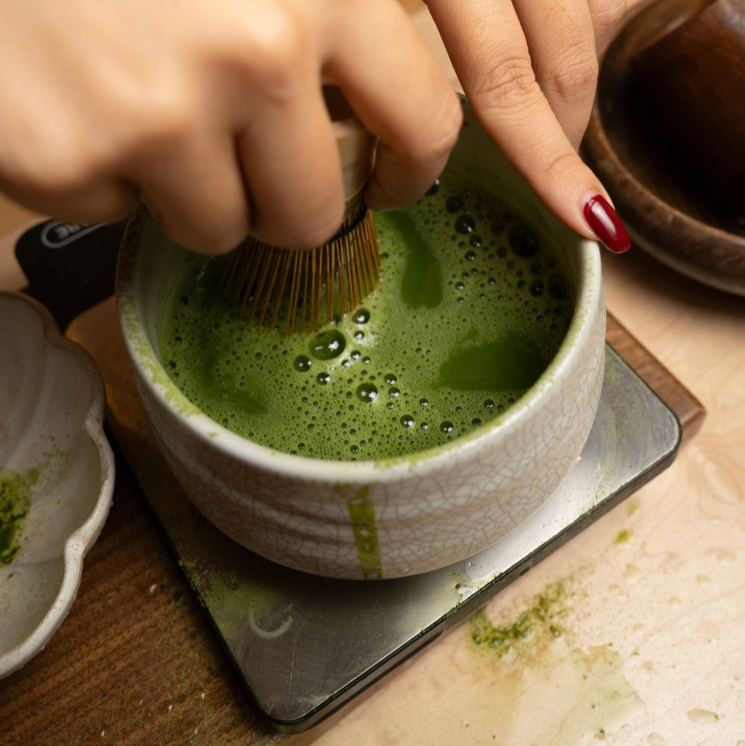 Preparing Japanese matcha by whisking green tea powder in a ceramic matcha bowl
