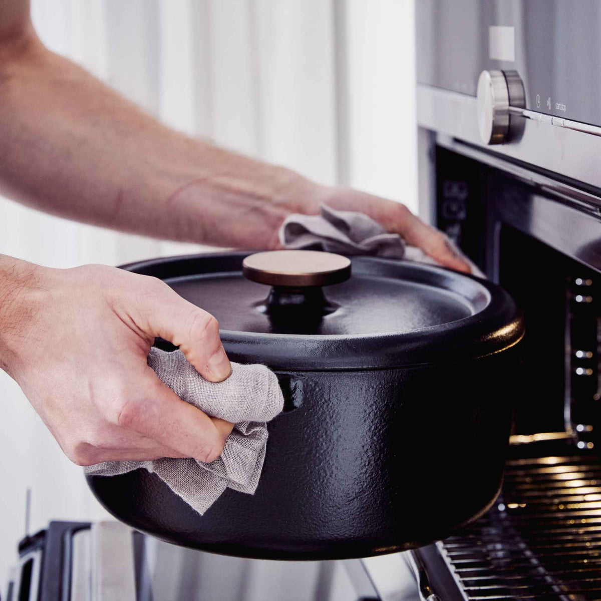 Hands placing the lid on an Alva black enameled cast iron Dutch oven on a stovetop