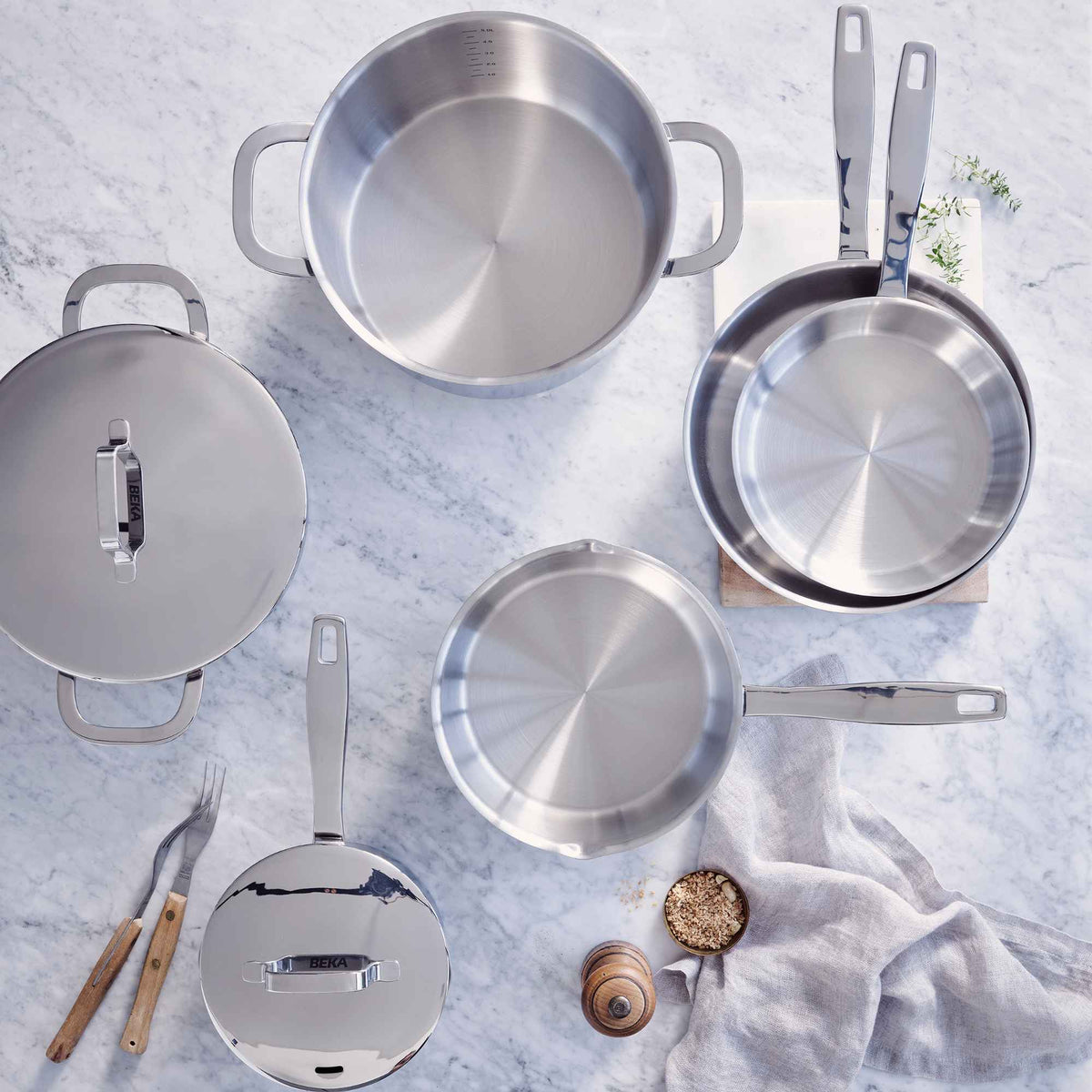 Alva stainless steel pots, pans and lids arranged on a light kitchen surface