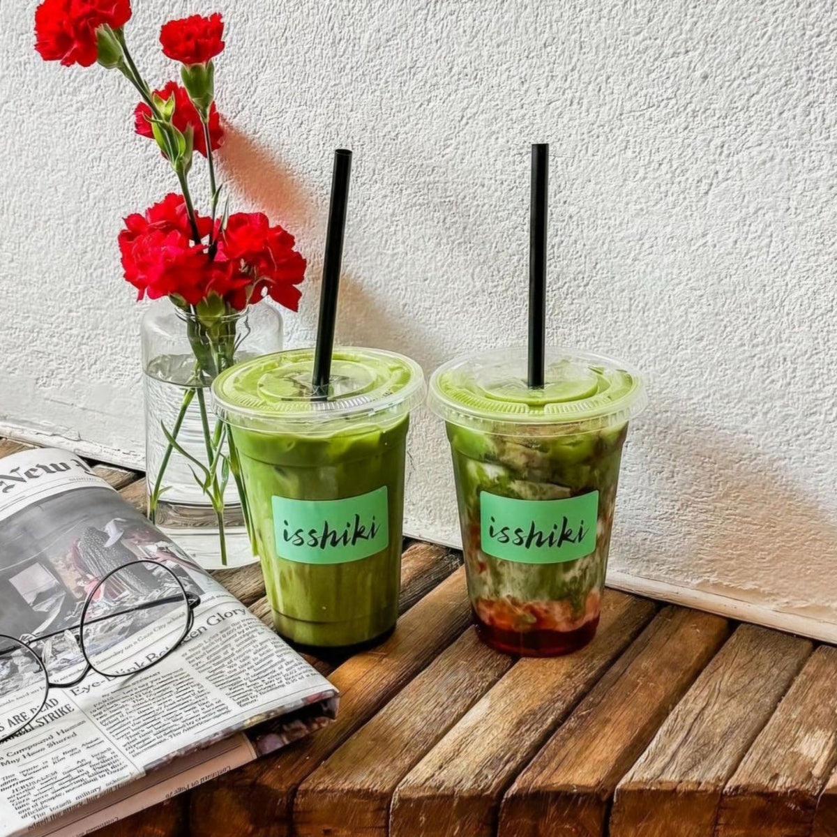 Two iced matcha drinks with straws served outdoors on a wooden table