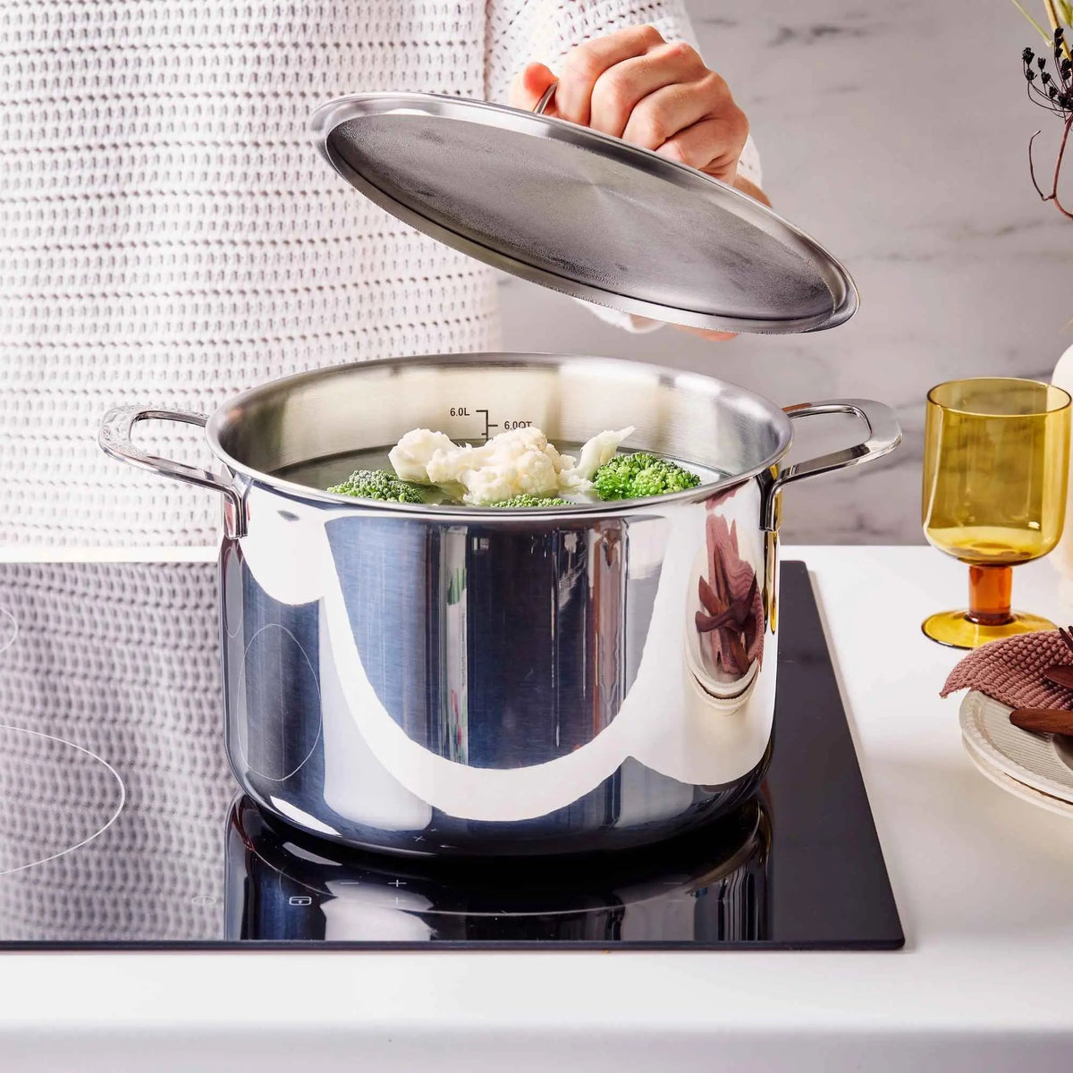 Home cook lifting the lid from an Alva stainless steel stock pot filled with vegetables