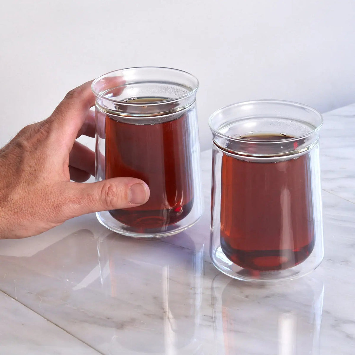 Two double-walled glass tea cups being held beside each other